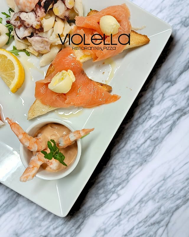 Antipasto di mare: salmone, scampi e tartare su piatto bianco